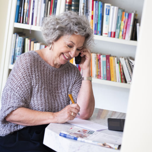Eine ältere Dame sitzt am Schreibtisch und telefoniert glücklich lächelnd